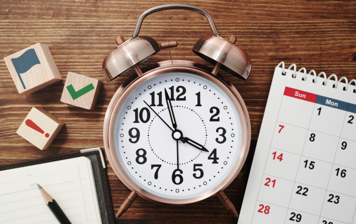 Bild mit Wecker und Kalender sowie einem Block und Stift als Sinnbild für Zeitmanagement