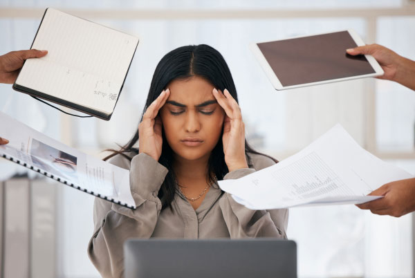 Frau, die mit Arbeitsaufgaben zugeschüttet wird als Zeichen von Burnout im Arbeitsalltag